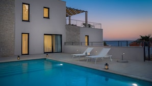 A modern pool area with two lounge chairs, a pool, and a view of the sea at dusk. - Luxury Villa Juliet with Heated Pool (Milna)