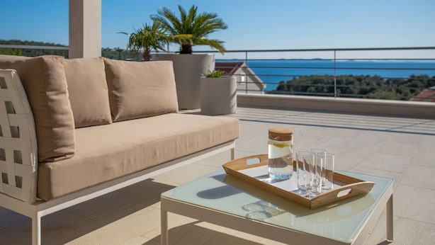 A balcony with a beige sofa, a glass coffee table, and a tray with a jar and glasses. - Luxury Villa Juliet with Heated Pool (Milna)