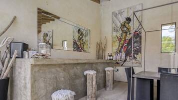 A rustic bar area with a concrete counter, wooden stools, and artwork on the walls.