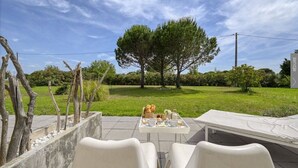 An outdoor patio with a table set for breakfast, surrounded by white chairs, a bench, and a lounge chair. - Mas Sainte Marie - Private Hot Tub Suites (Saint-Laurent-d'Aigouze)