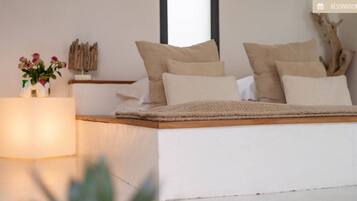 Ein modernes Schlafzimmer mit einem Bett, Kissen, einem Nachttisch und einer Blumenvase.