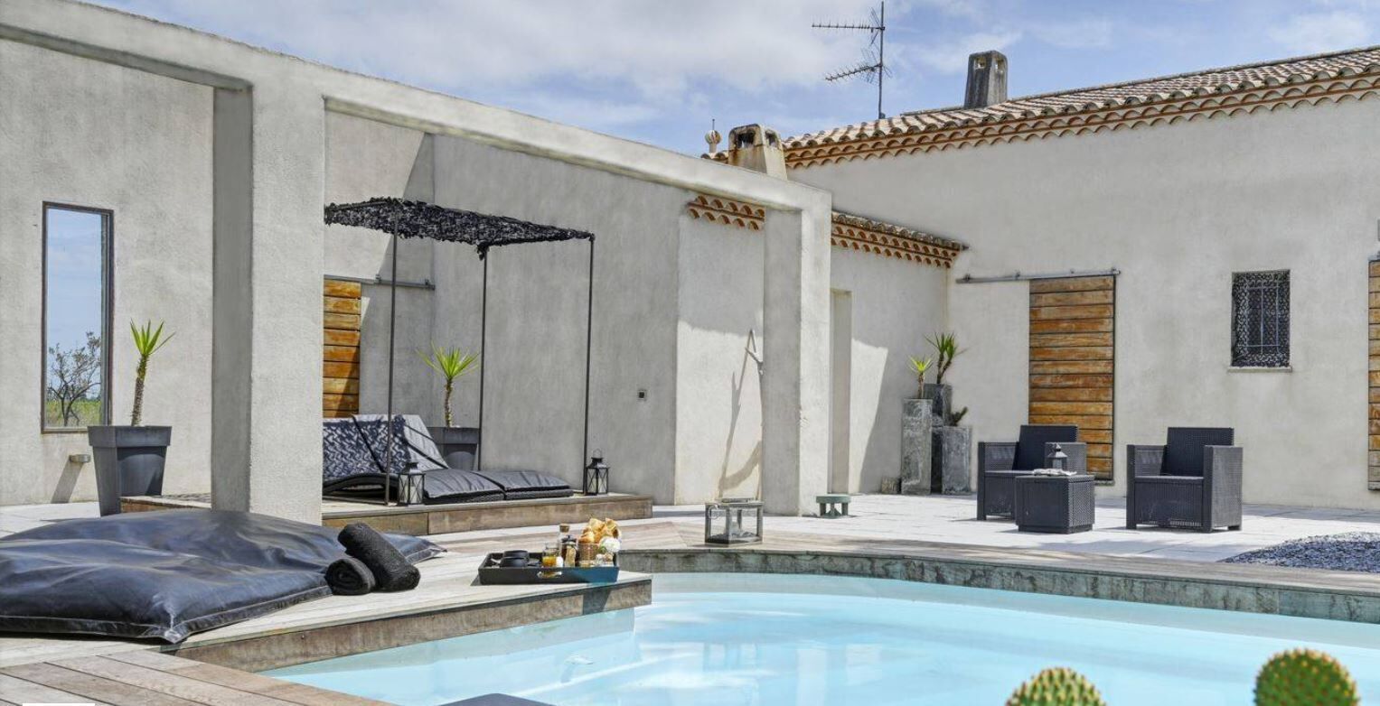 A modern outdoor pool area with a lounge chair, a small table with drinks, and a wooden bench.