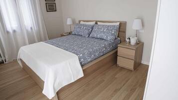 A neatly made bed with a patterned bedspread and pillows, wooden nightstands with lamps, and a white wall with two framed pictures.