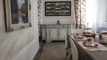 A dining area with a white cabinet, floral curtains, and a framed landscape painting.