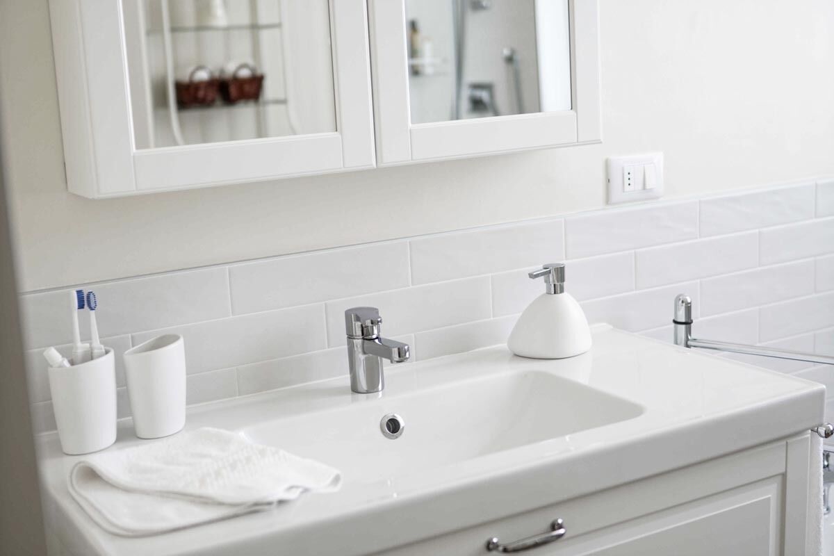 A white bathroom with a sink, two faucets, a mirror, and a towel.