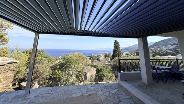 A covered outdoor area with a view of the sea and a stone-paved patio.