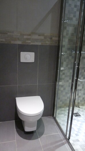 Un baño moderno con inodoro, cabina de ducha de vidrio y panel de control en la pared.