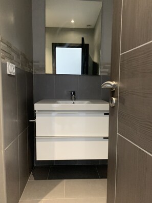 A modern bathroom with a white vanity, a mirror above the sink, and a door with a silver handle.