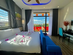 A modern hotel room with a large bed, a blue sofa, a desk, and a view of the city. - The Night Market Villa (Da Nang)