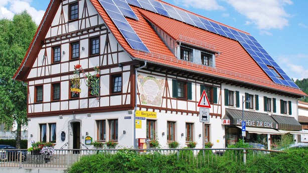 A traditional half-timbered building with solar panels on the roof, a sign for 'Biergarten', and a 'Parking' sign.