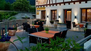 An outdoor seating area with tables and chairs, potted plants, and a sign indicating a parking area.