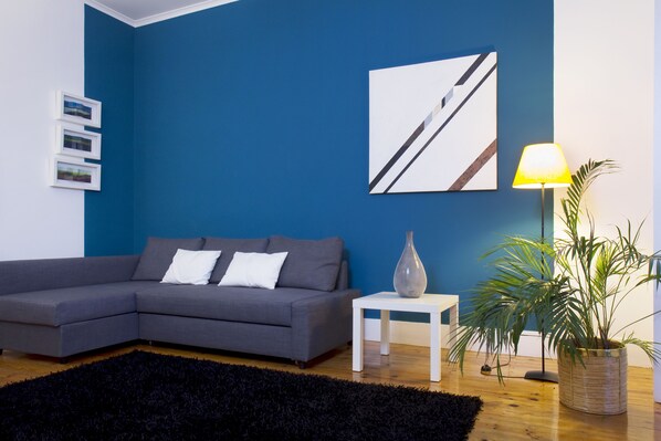 Una sala de estar moderna con un sofá modular gris, un tapete negro, una mesita blanca, una lámpara y una planta en maceta.