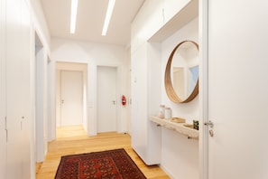 A hallway with a wooden floor, white walls, a round mirror, and a small shelf with toiletries. - FLH Chiado Amazing Flat (Lisbon)