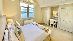 A bedroom with a large bed, a desk, a chair, and a window with a view of a body of water. - Beautiful 4 bed lakeside lodge in the Cotswolds. Private deck & STUNNING views (South Cerney)
