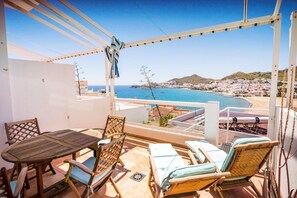 Un balcone con tavolo e sedie, vista su una spiaggia e una cittadina costiera.