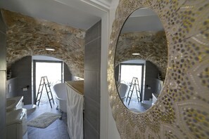 A bathroom with a stone wall, a white bathtub, and a large ornate mirror.