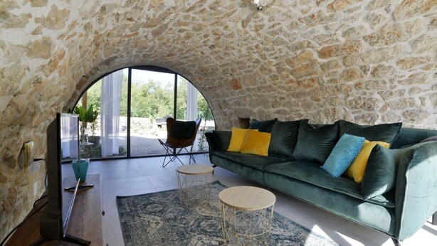 A cozy living room with a stone wall, a green sofa with yellow cushions, a wooden coffee table, and a large arched window.
