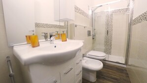 Un baño con un lavabo blanco, dos dispensadores de jabón amarillos, un inodoro blanco y una cabina de ducha de vidrio.
