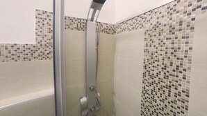 Ducha con puerta de vidrio y pared revestida de mosaicos.