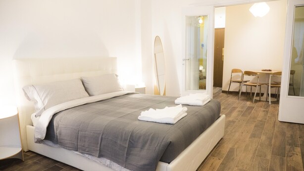 Un dormitorio moderno con una cama grande, una mesita de noche, una silla y una tabla de surf apoyada en la pared.