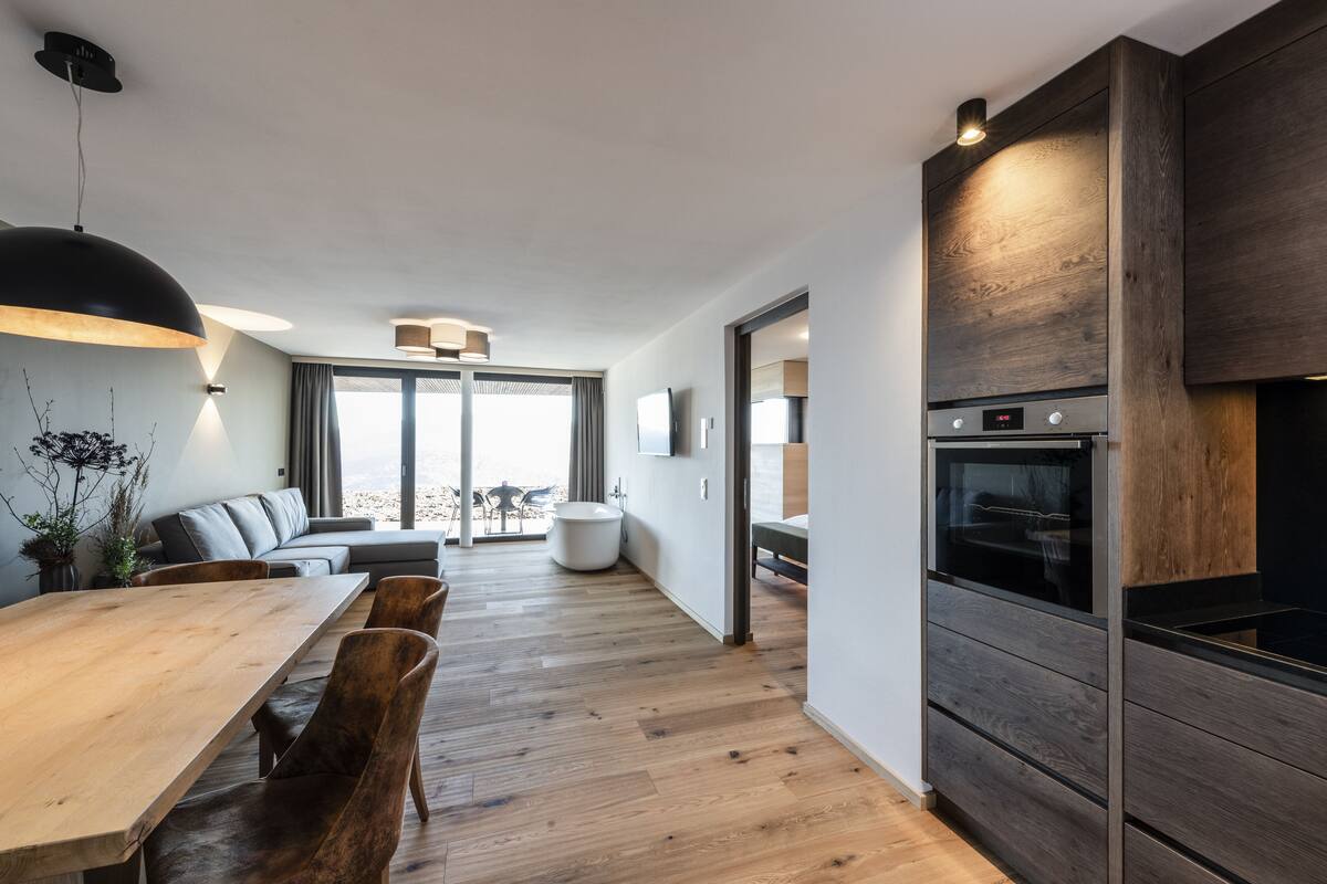A modern kitchen with a wooden dining table, chairs, and a built-in oven.