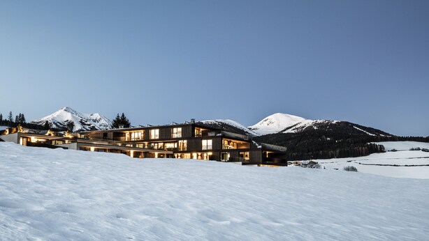 A modern multi-story building with large windows and a snow-covered mountain in the background. - Panorama Living Dolomites (Rio di Pusteria)