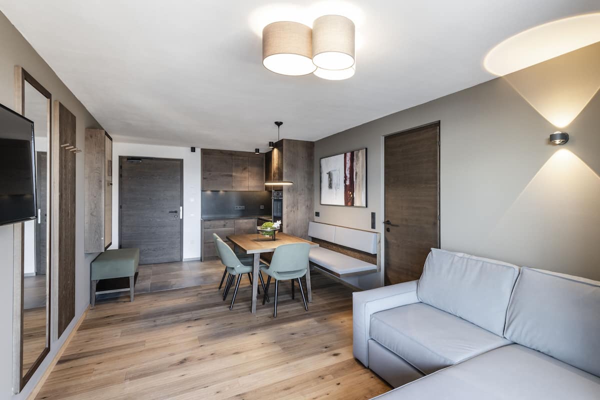 A modern kitchen with wooden cabinets, a dining table with chairs, and a light-colored sofa.