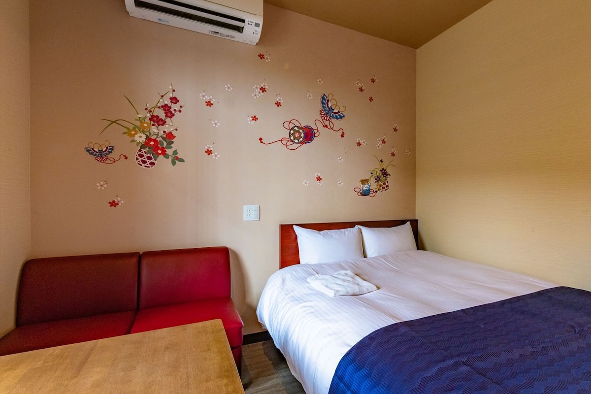 A hotel room with a bed, a red sofa, a small table, and wall decorations.