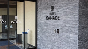 L’extérieur de l’hôtel Kanade se distingue par sa façade moderne en briques, son entrée en verre et un panneau indiquant qu’il est accessible aux personnes à mobilité réduite.