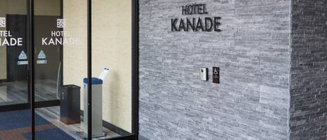 Hotel Kanade set fra ydersiden med en moderne murstensfacade, glasindgang og et skilt for tilgængelighed med kørestol.