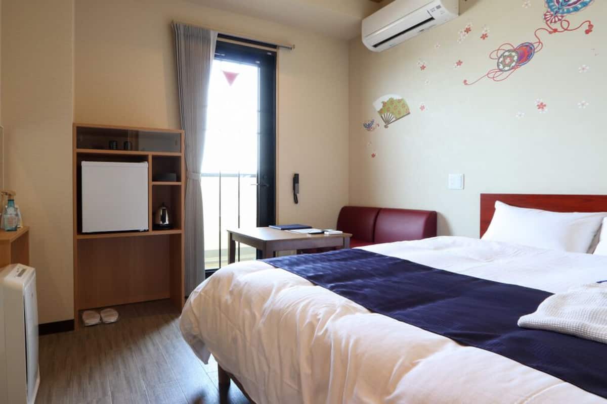 A hotel room with a bed, a desk, a chair, a wardrobe, a radiator, and a window with curtains.