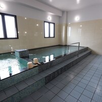 A swimming pool with tiled walls and a tiled floor, two chairs, and a small table.