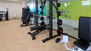 Une salle de sport équipée de matériel de musculation, d’un banc et d’un mur orné d’une fresque colorée.