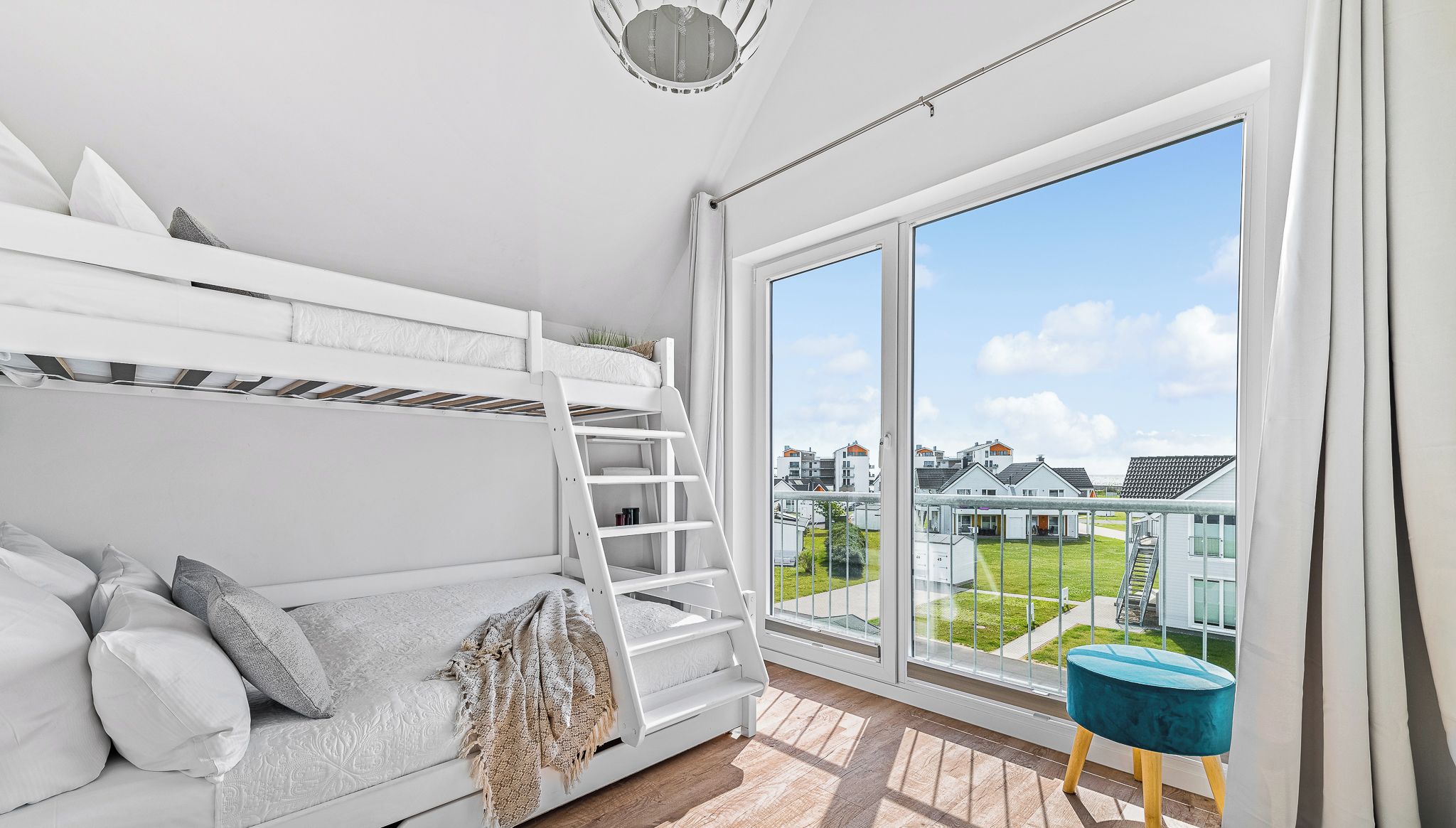 A modern bedroom with a bunk bed, a small stool, and a large window offering a view of the neighborhood.