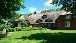 Ein traditionelles, mit Stroh gedecktes Haus mit zahlreichen Fenstern und einem gepflegten Garten.