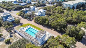 Vista aérea de uma área residencial costeira, com casas, uma piscina e uma praia ao fundo.
