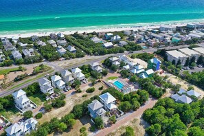 An aerial view of a coastal residential area with houses, a swimming pool, and a beach.