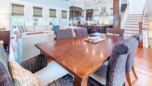 Uma sala de estar ampla com uma grande mesa de jantar de madeira, cadeiras de vime e um sofá com almofadas estampadas.