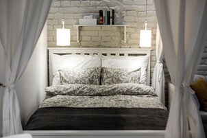 Una cama con cabecera blanca, ropa de cama estampada y una estantería con libros y una caja blanca pequeña.