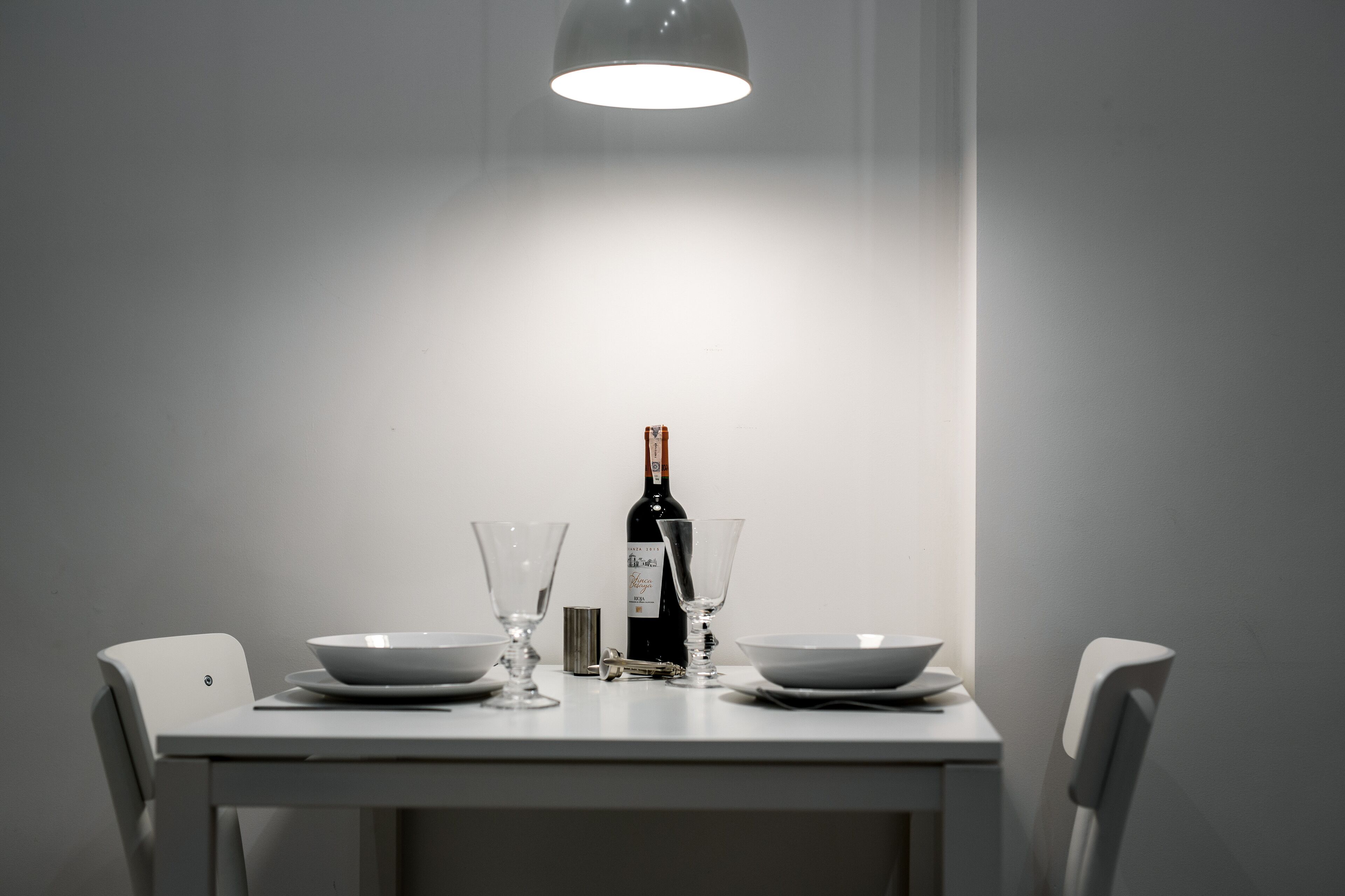 A dining table with two white chairs, a bottle of wine, and two wine glasses.