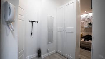 A hallway with white walls, a white phone, a coat rack, and a door leading to a room with a stone wall and a sofa.
