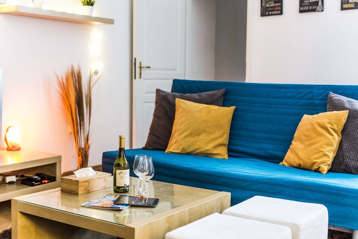 A living room with a blue sofa, a wooden coffee table, and a white ottoman.
