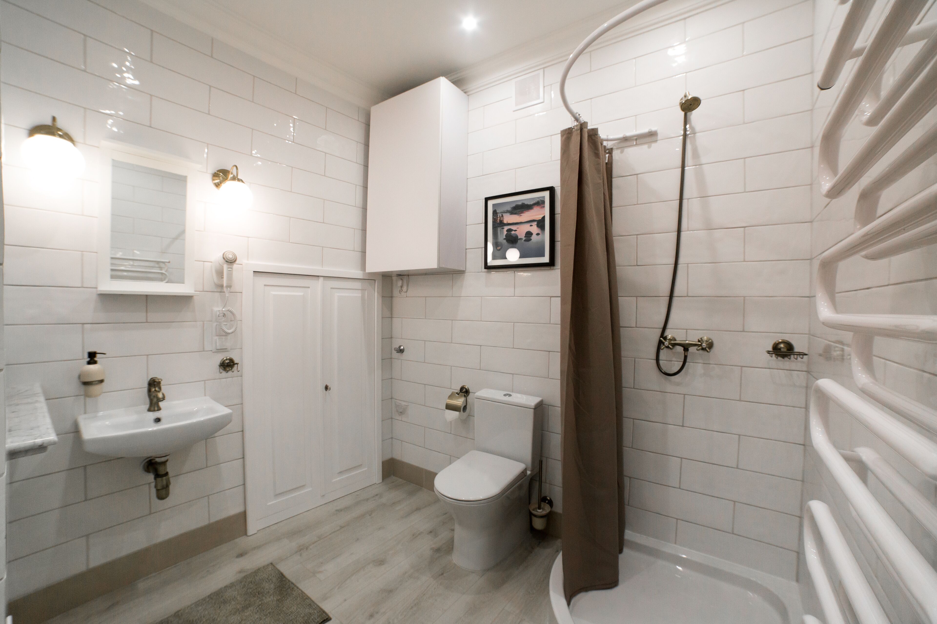 Une salle de bain avec des carreaux blancs, un lavabo, des toilettes, une douche avec un rideau et un tableau encadré au mur.
