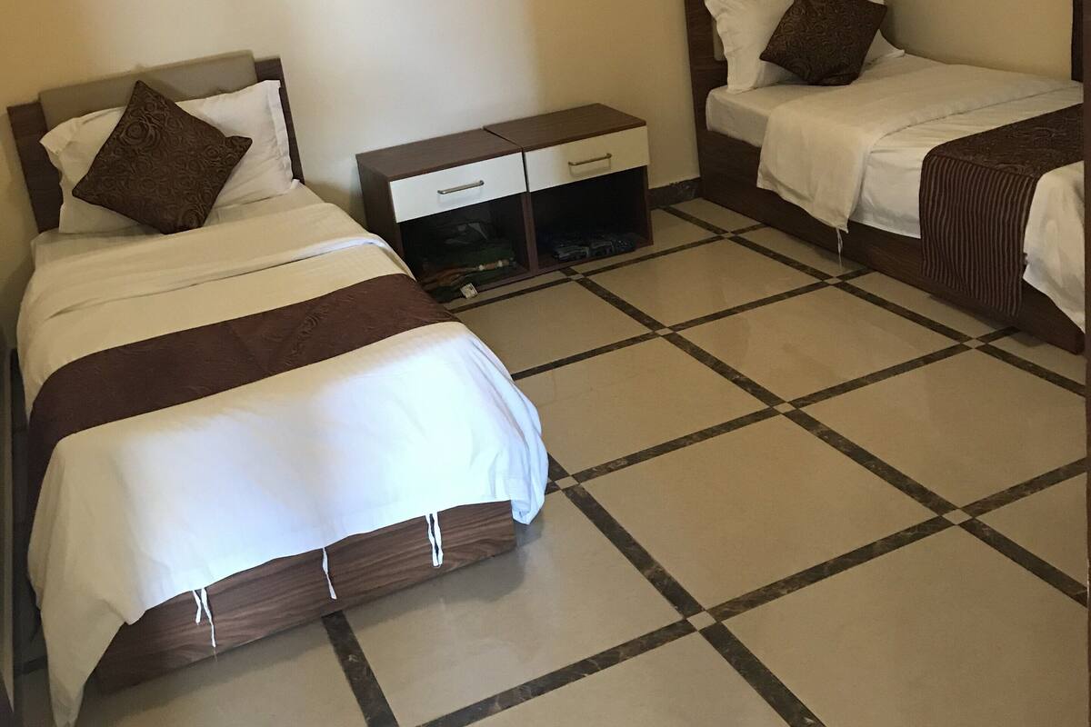 A hotel room with two beds, a small bedside table, a wardrobe, and a tiled floor.
