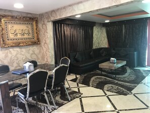 Uma sala de estar moderna com um sofá de couro preto, uma mesa de jantar de vidro com cadeiras, uma mesa de centro e um tapete estampado.
