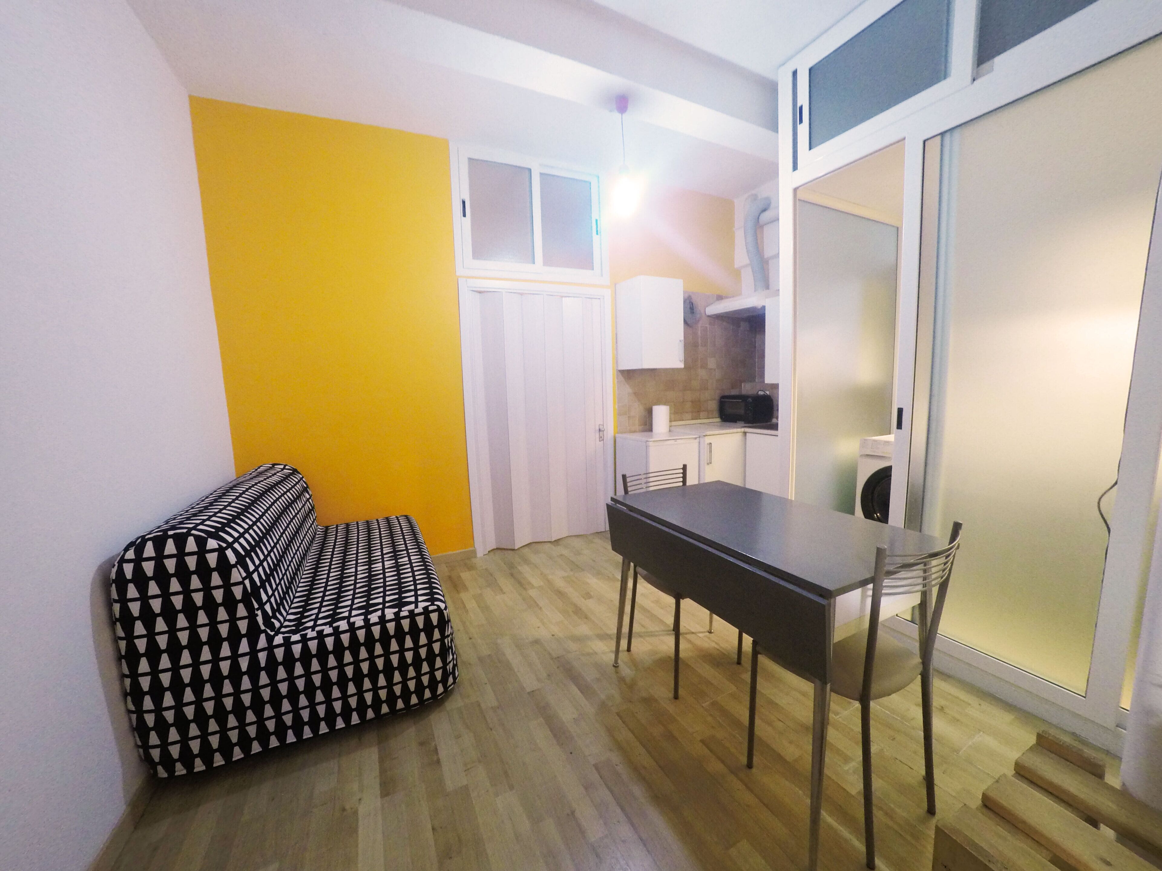A compact living space with a sofa, a dining table, and a kitchen area.