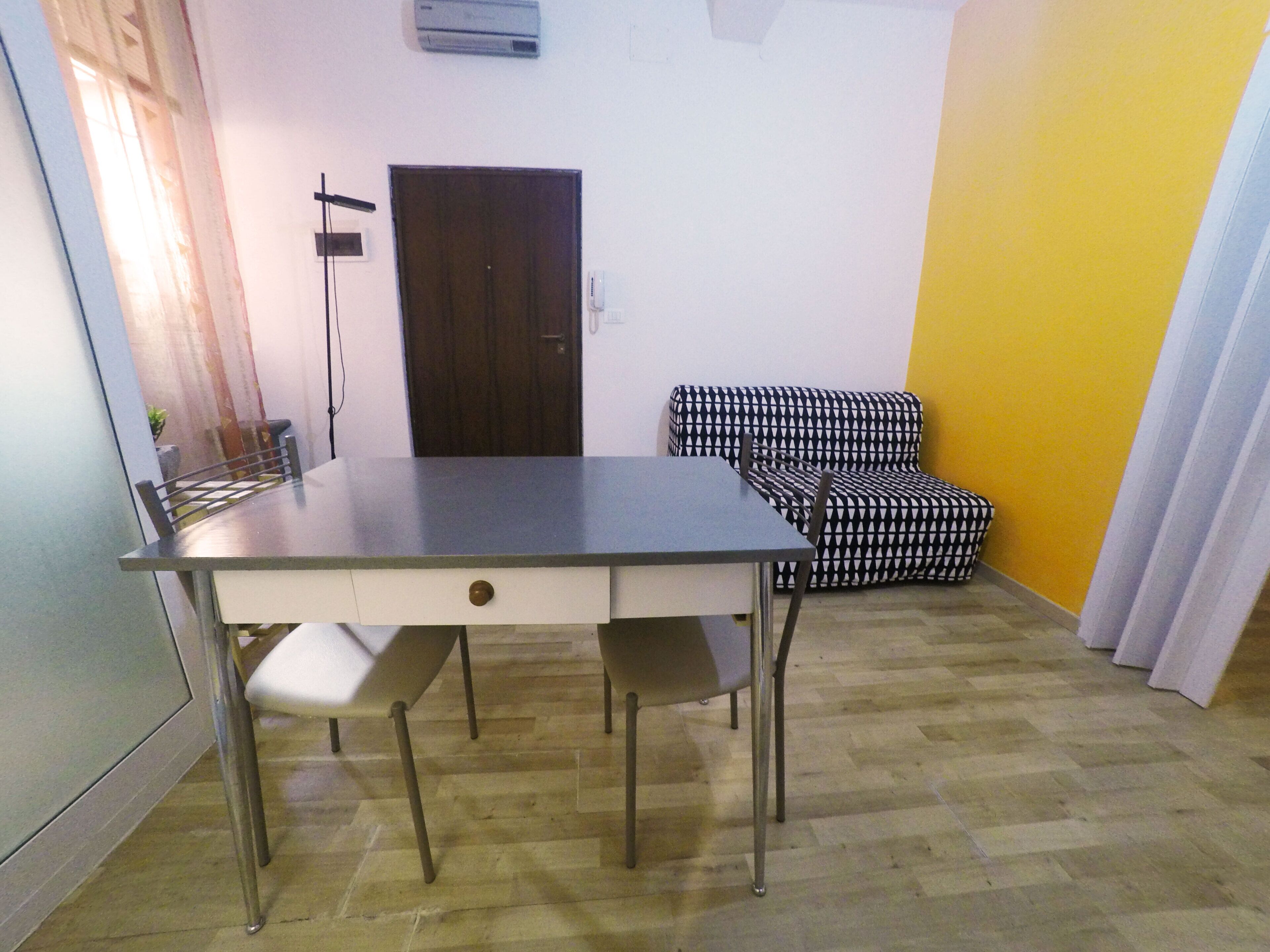 Uma área de refeições com mesa e cadeiras, um sofá, uma porta e um aparelho de ar condicionado.