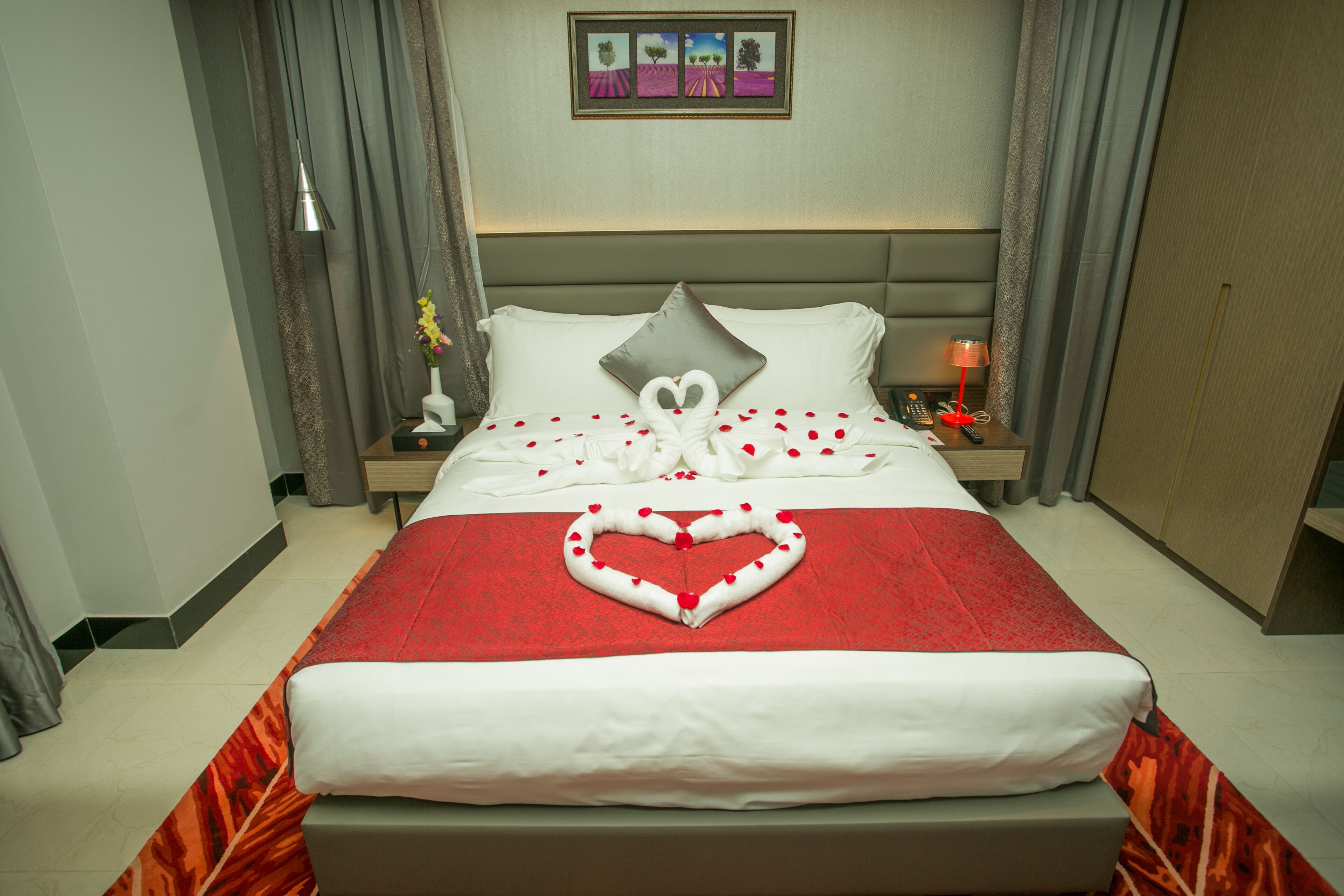 A hotel room with a neatly made bed, a nightstand with a lamp, and a painting on the wall.