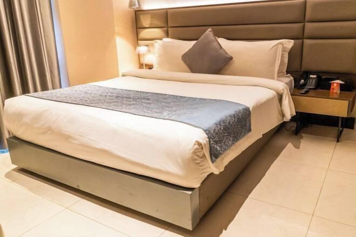 Una habitación de hotel moderna con una cama grande, una mesita de noche con lámpara y otro mesita con teléfono.