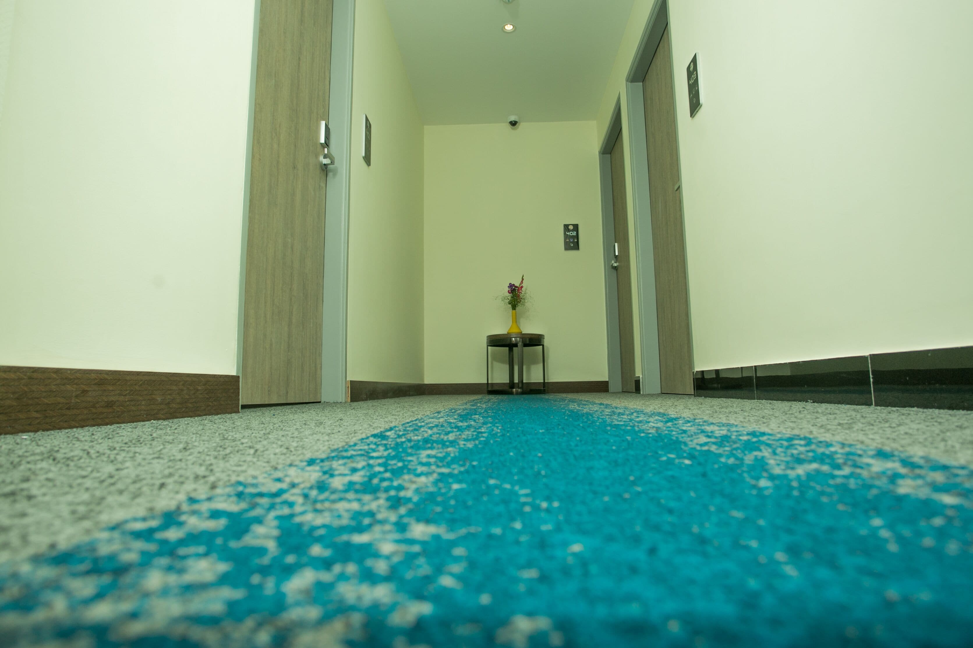 A hallway with a blue carpet, a small table with a vase, and a door on the right.